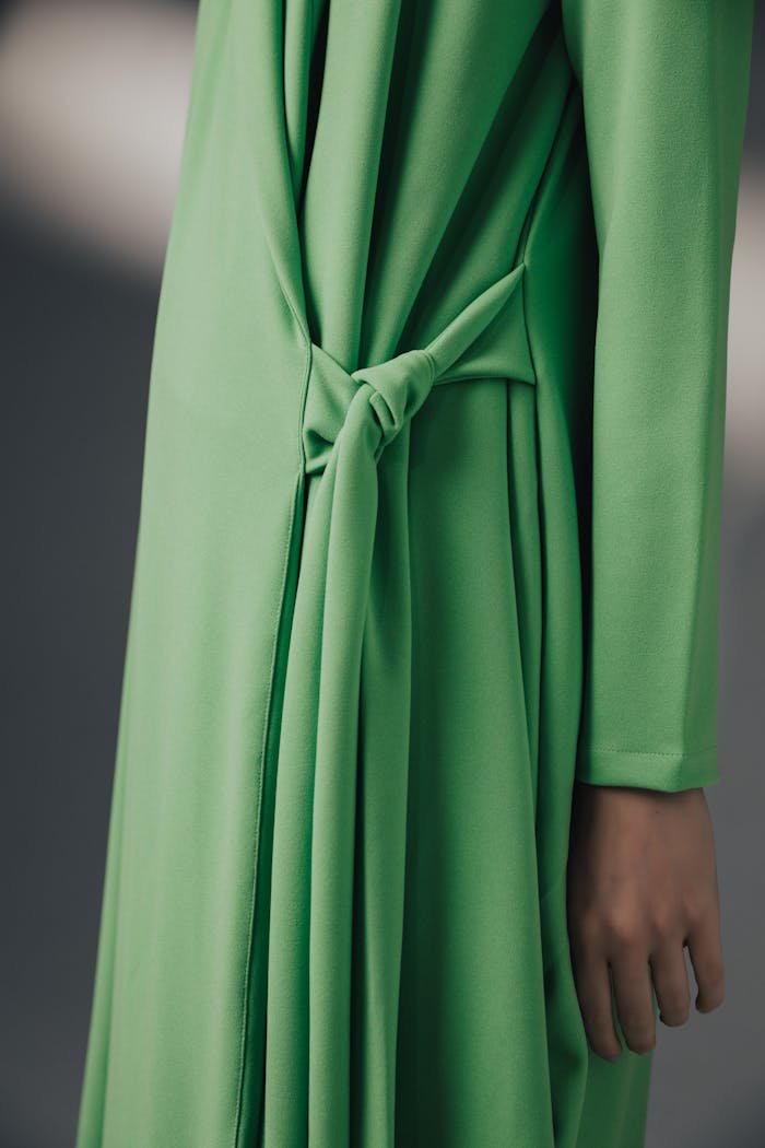 Close-up view of a woman wearing a green dress with a stylish knot detail, showcasing modern fashion.